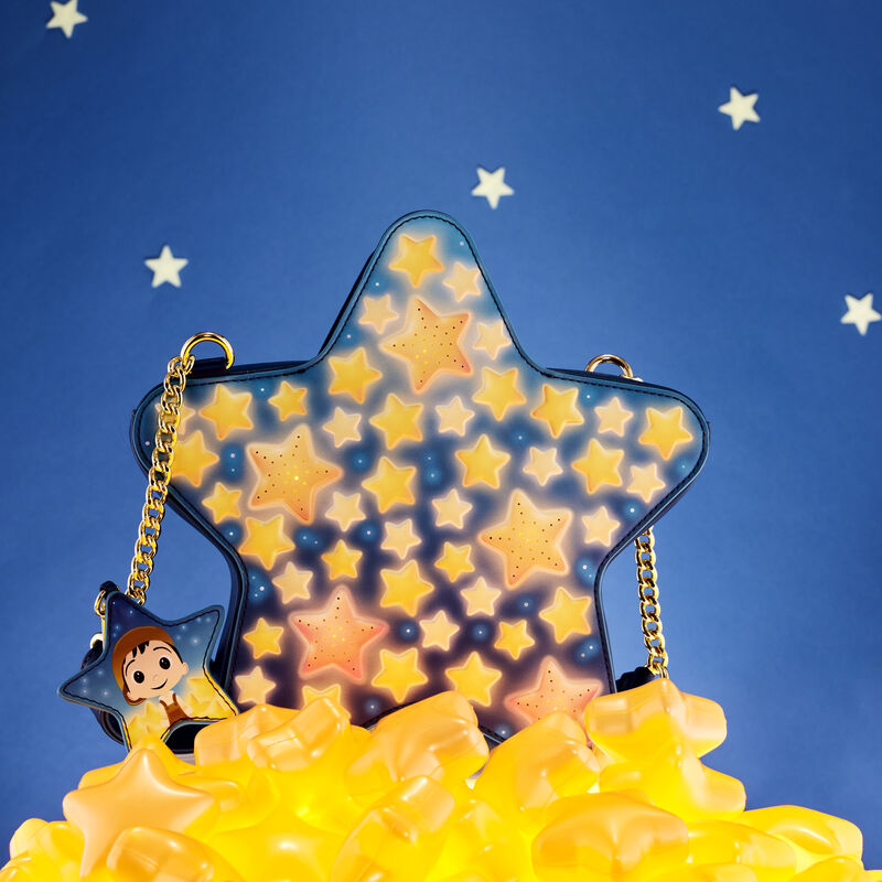 Star-shaped La Luna crossbody bag sitting on a pile of yellow glowing stars against an evening sky background. 